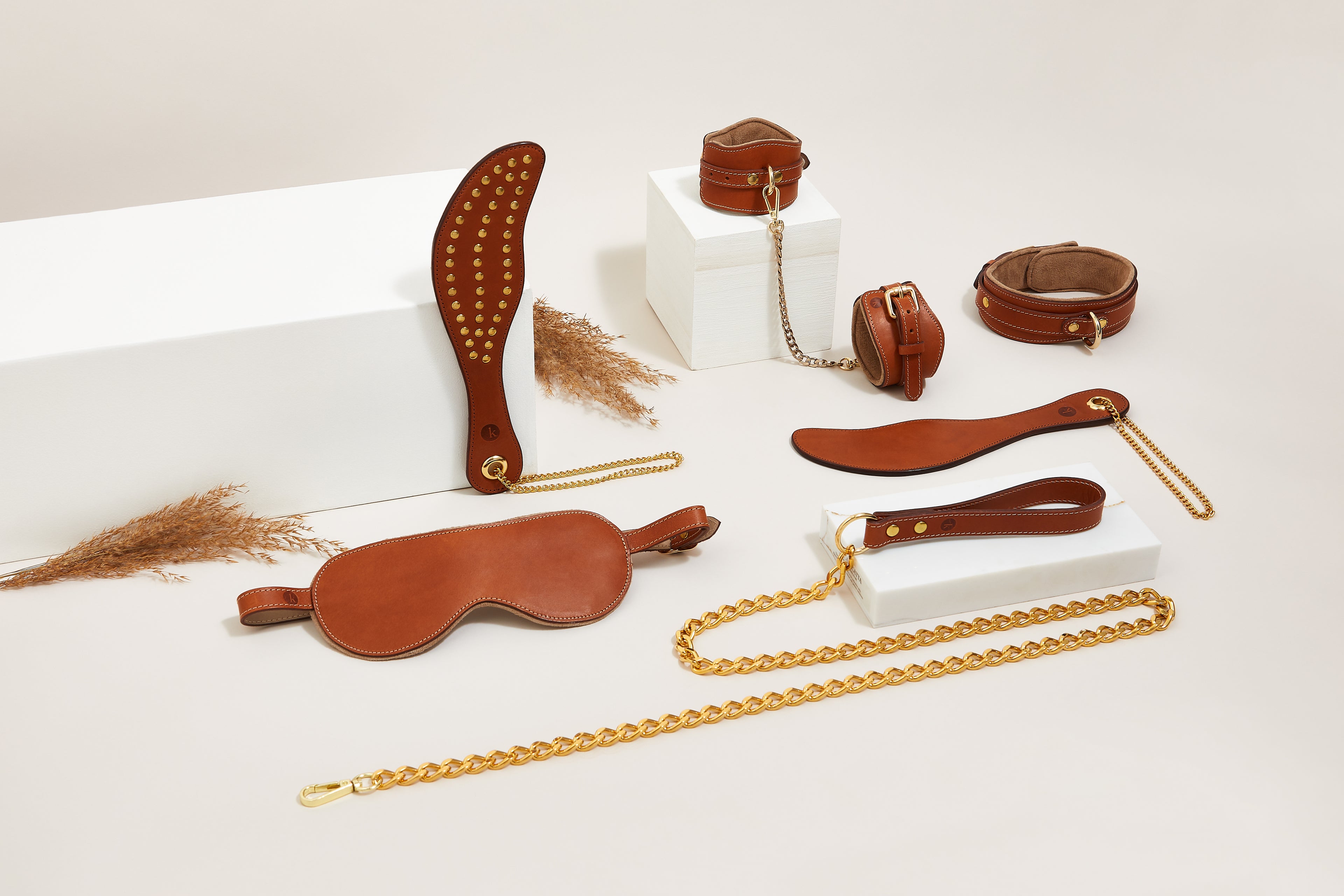 Luxury tan leather BDSM set for bondage play including wrist restraints, collar, spanking paddle and blindfold