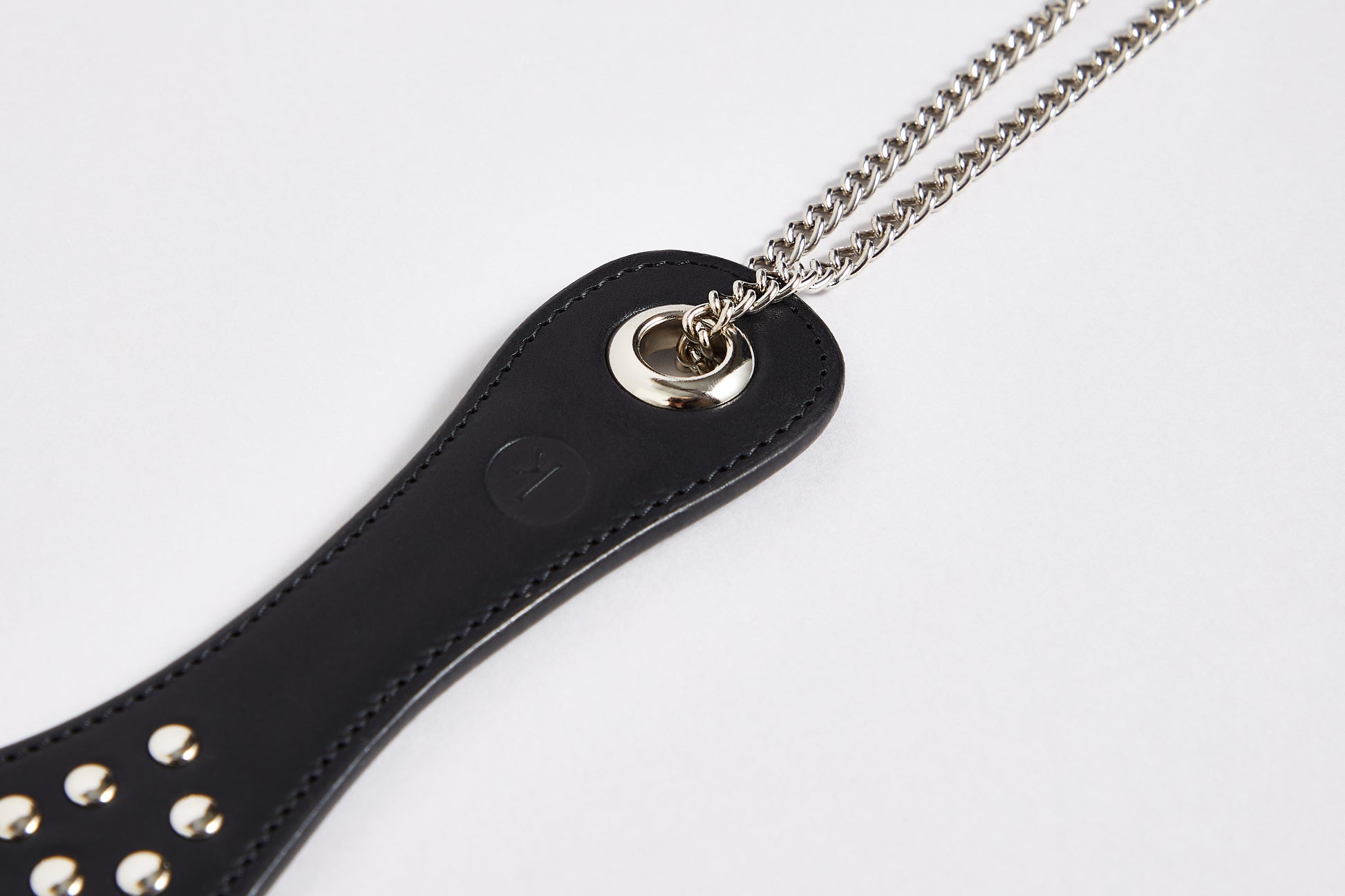 Detail of studded black spanking paddle with silver wrist chain